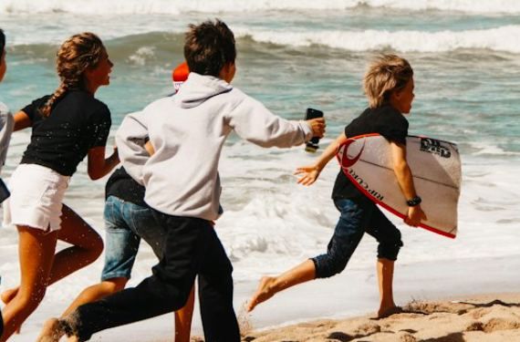 Children running into the sea, one carrying a bodyboard